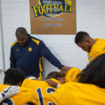 Phoenix College coaches lead players in prayer before they take the field. This is a tradition for the Bears before every game. (Photo by Chris Lindsay)
